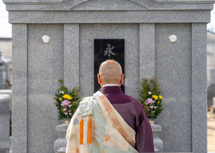 A Buddhist monk paying his respects at a flower-adorned grave in Japan.